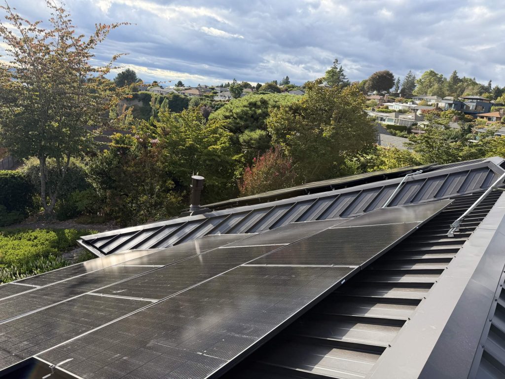 West Seattle home with a new dark bronze standing seam metal roof, solar array, garden, and water view