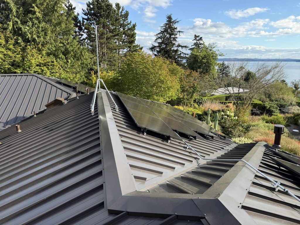 Dark bronze Nu-Ray Series 2000 standing seam metal roof with a 17.1 kW solar array overlooking a tree-filled garden and water in West Seattle, WA
